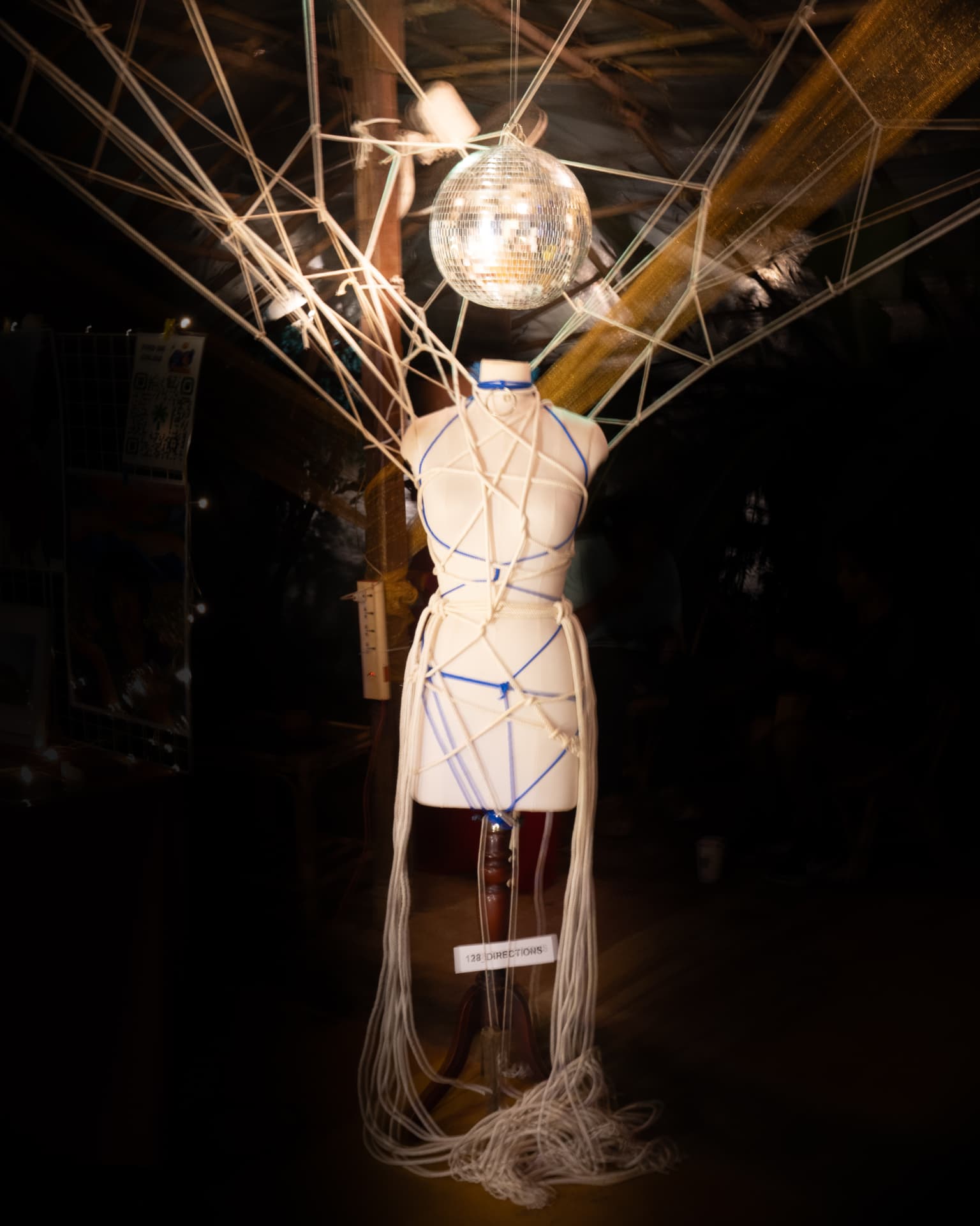 Rope art installation on a mannequin beneath a mirror ball and '128 DIRECTIONS' sign