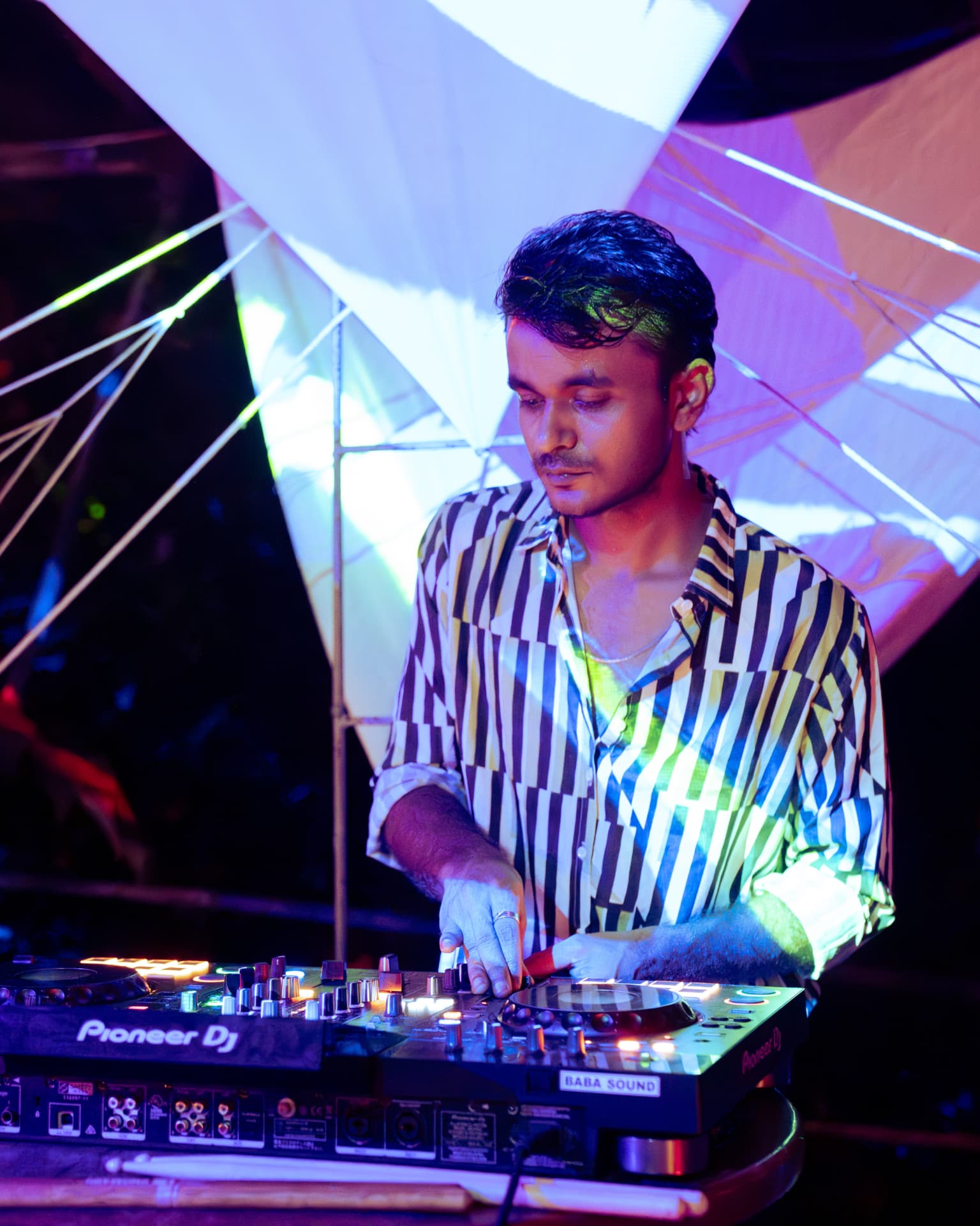 DJ mixing under stretched canvas sails and neon projections