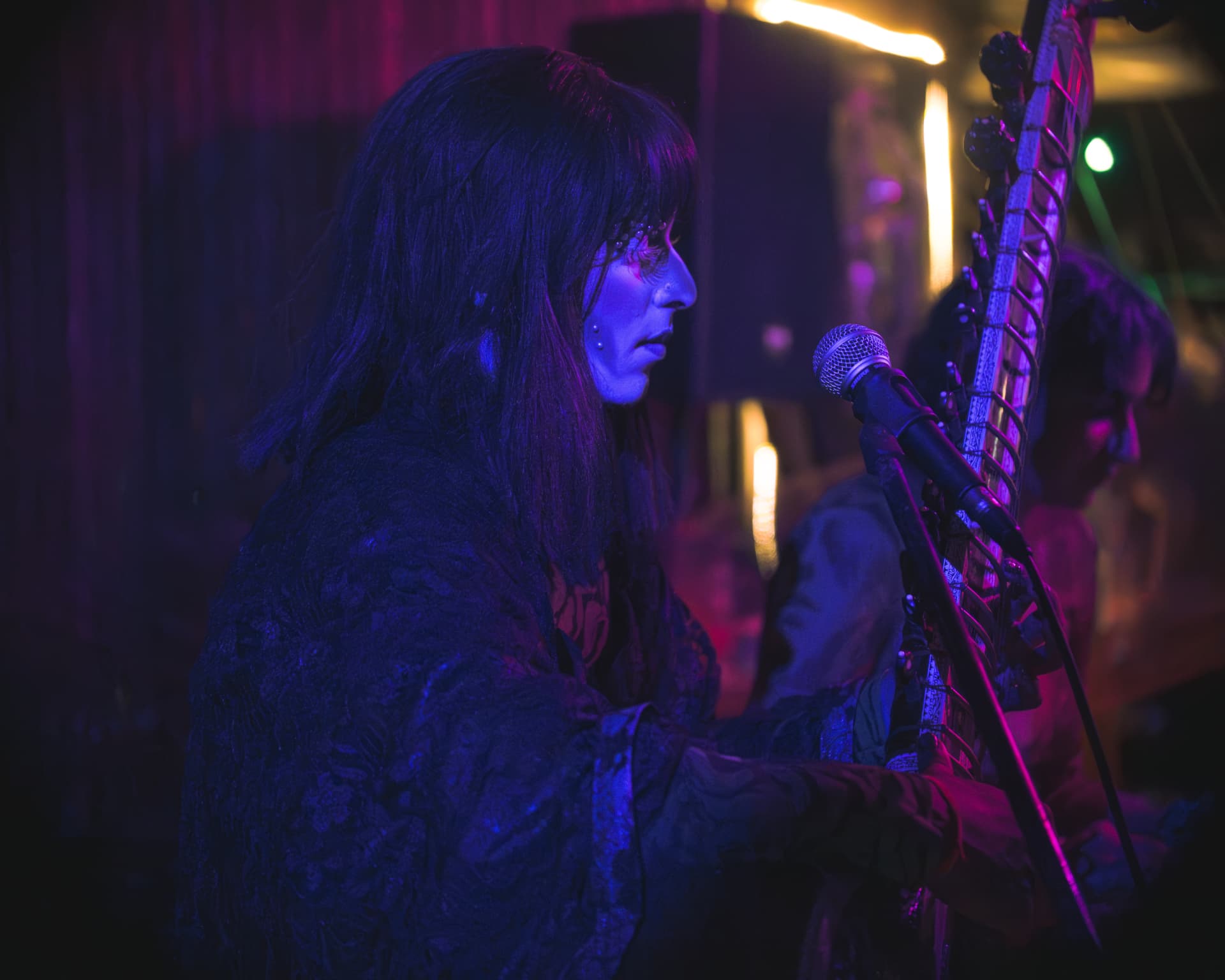 Performer in profile beside a sitar in blue stage light