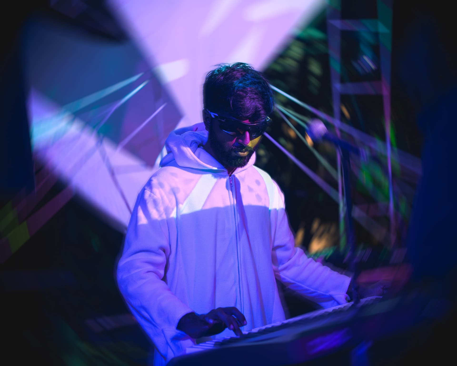 Keyboardist in a white hoodie lit by projection beams
